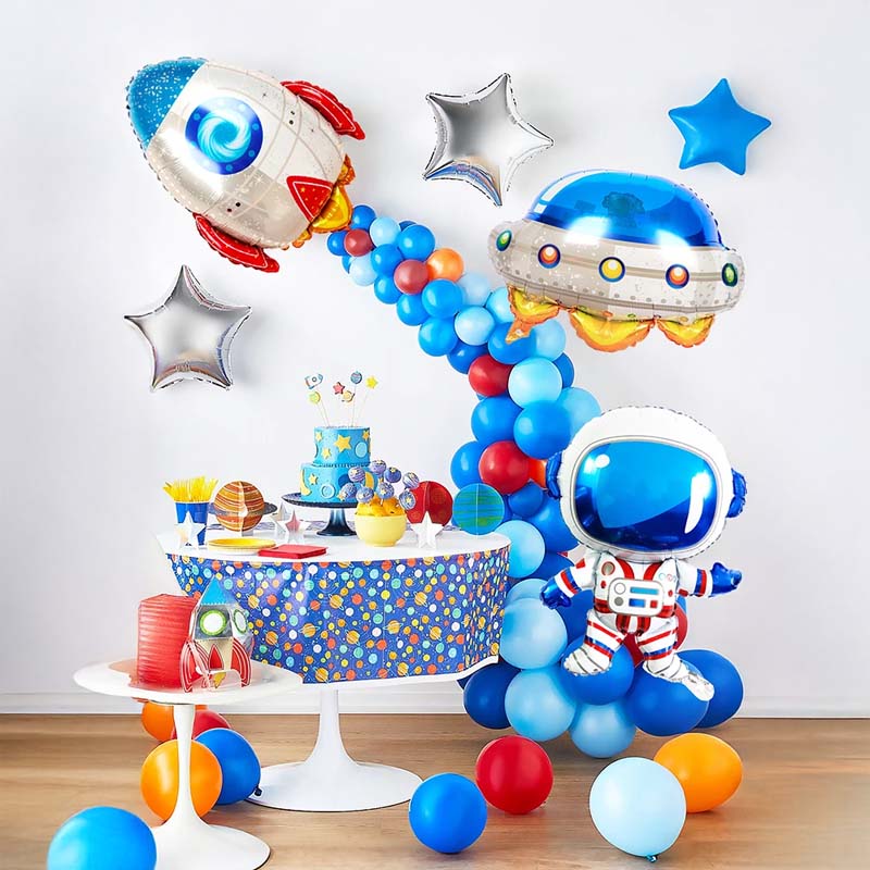 Space-themed birthday party setup with balloons, cake, and decorations on a wooden table.