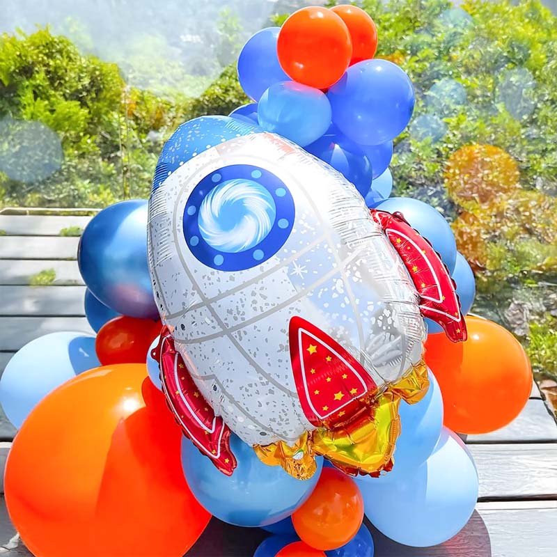 Balloon arrangement with a rocket-shaped balloon and colorful balloons on a wooden surface with a natural background.