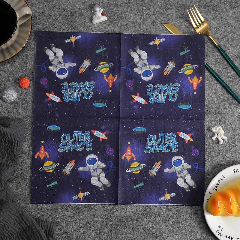 A piece of fully opened space-themed napkin placed on a gray surface with cutlery and décor items.